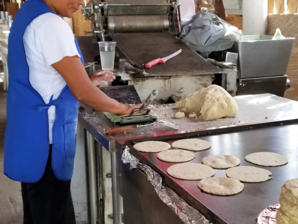 Lady pressing tortillas by hand.