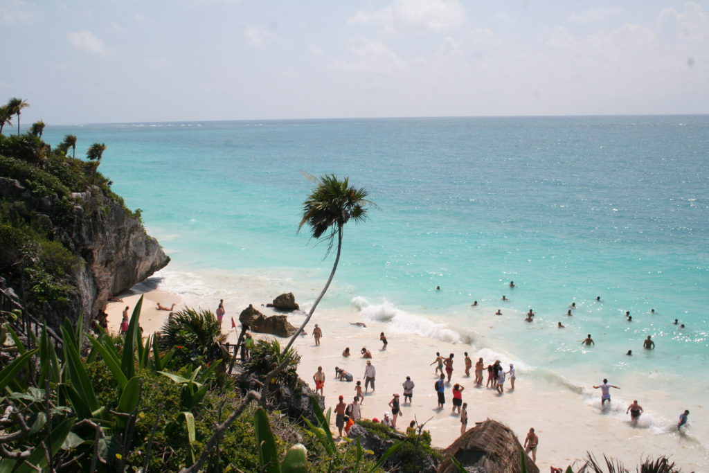 People enjoying the blue water and white sandy beach at Tulum, Mexico