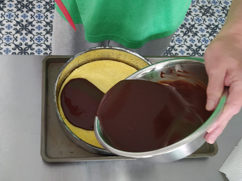 Pour chocolate ganache over cheesecake